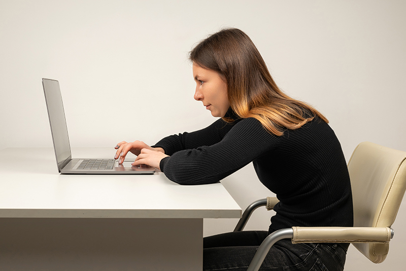 Vrouw in zwarte kleding werkt op haar laptop met een gegogen rug en krijgt hierdoor hoge rugklachten