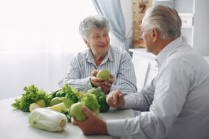 Man en een vrouw met artrose zitten aan een tafel met groenten en fruit die vitamine k bevatten.